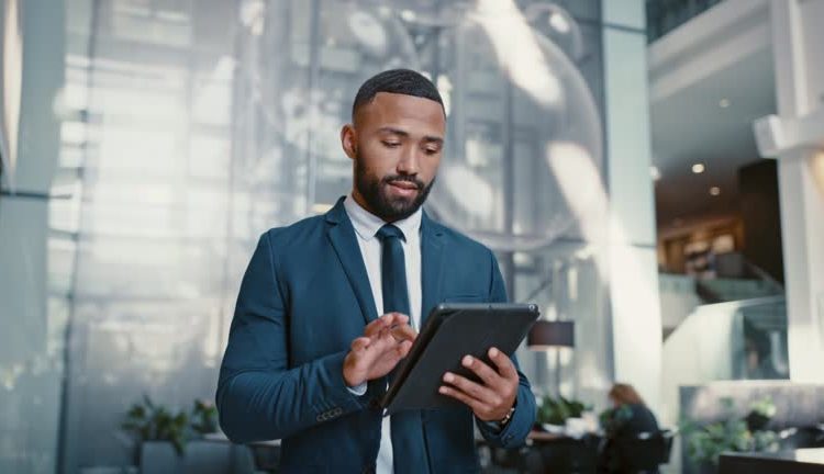 gettyimages-1436378050-640x640 Businessman working on a digital tablet while walking in a corporate office. Marketing professional and black man doing research on the internet or a website with a mobile device for startup project